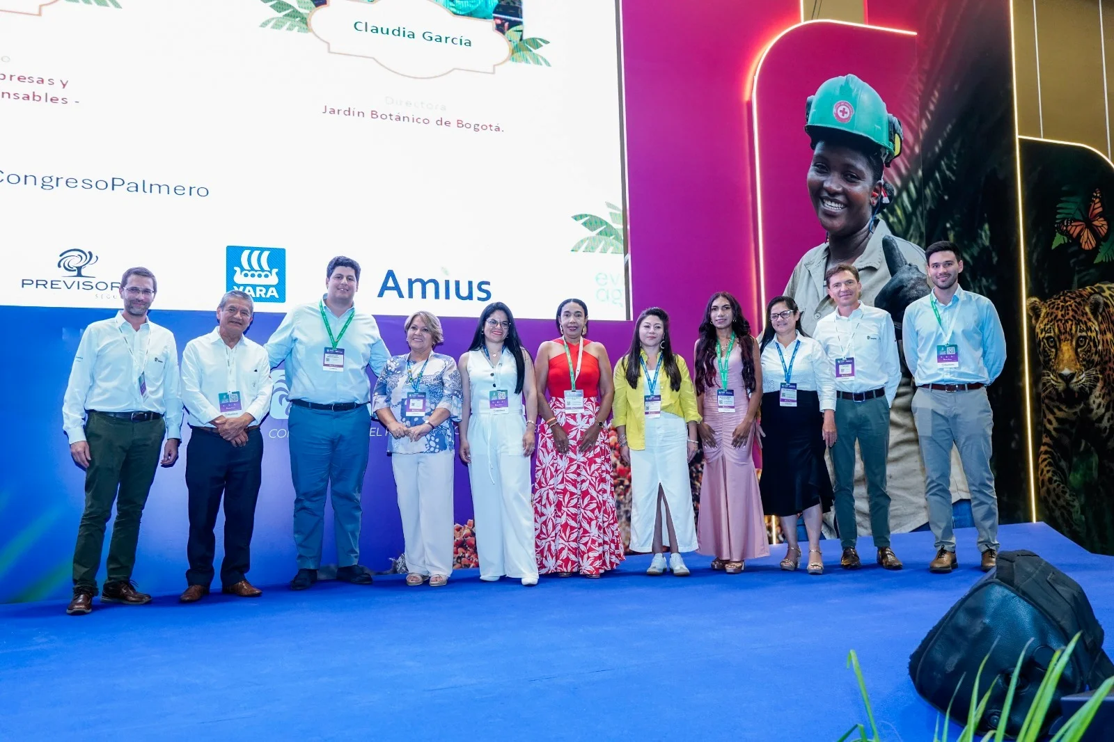 Grupo de diez personas de pie en un escenario posando frente a una pantalla de presentación